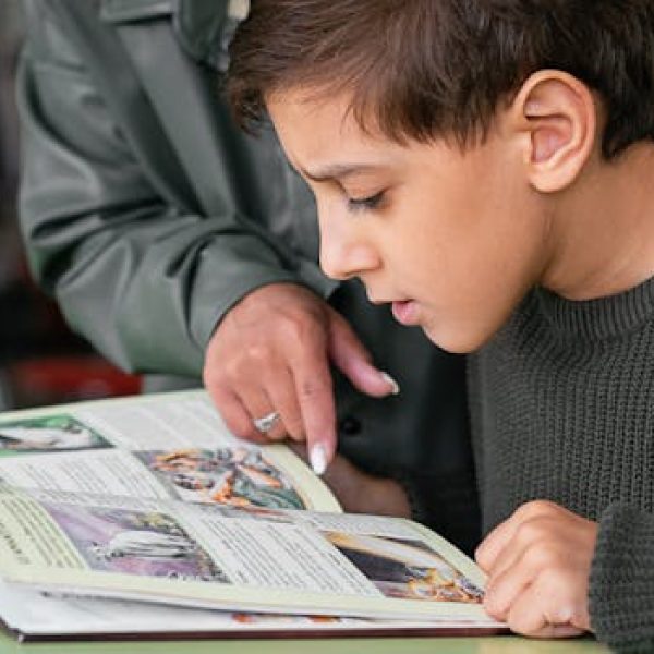 Boy concentrating on reading as adult points out text in a book.